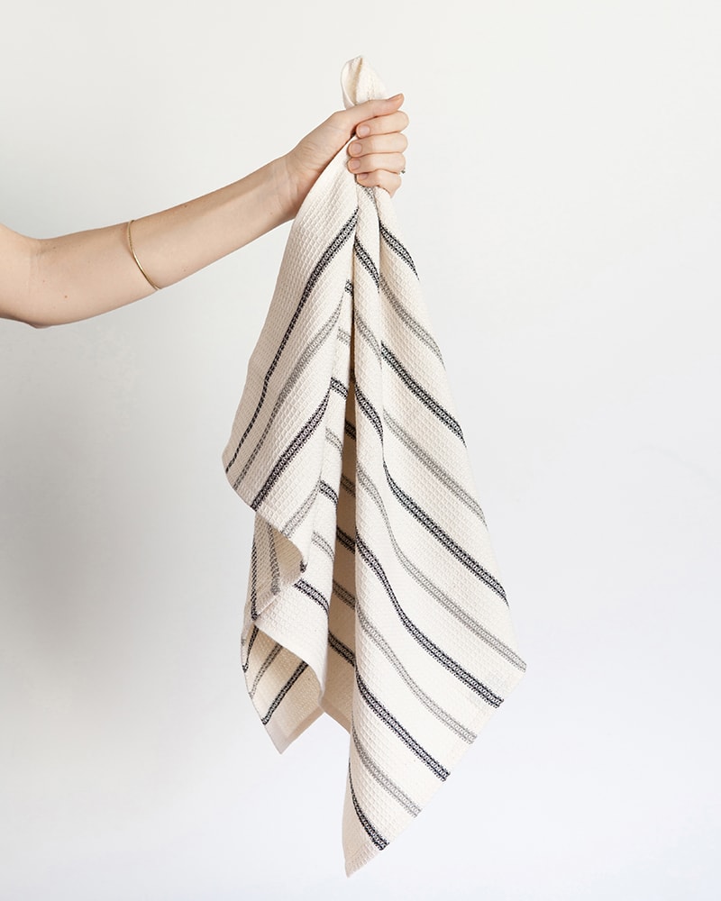 A hand holding the Mungo Linen and Cotton Waffle Weave Kitchen Towel in Black and Grey Stripe.