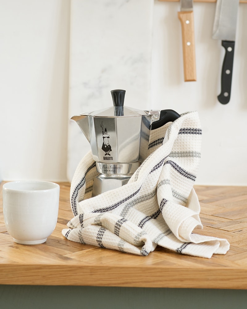 The Mungo Linen and Cotton Waffle Weave Kitchen Towel in Black and Grey Stripe, pictured in kitchen with a Bialetti and mug,