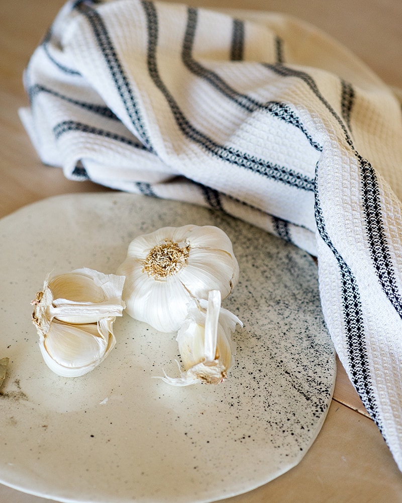 Mungo Linen and Cotton Waffle Weave Kitchen Towel in Black Stripe pictured with garlic and a ceramic platter.
