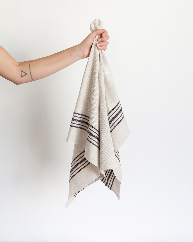 A hand holding a Mungo Linen Kitchen Utility Cloth in Natural. Made with all natural fibres on the looms at our mill in Plettenberg Bay.