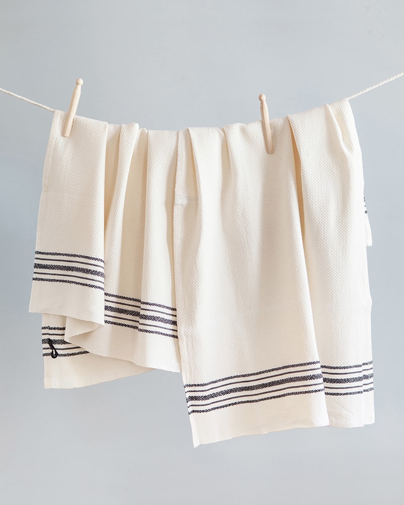 The Mungo Linen Kitchen Utility Cloths in Ecru, hung with pegs on a washing line. Made with all natural fibres on the looms at our mill in Plettenberg Bay.