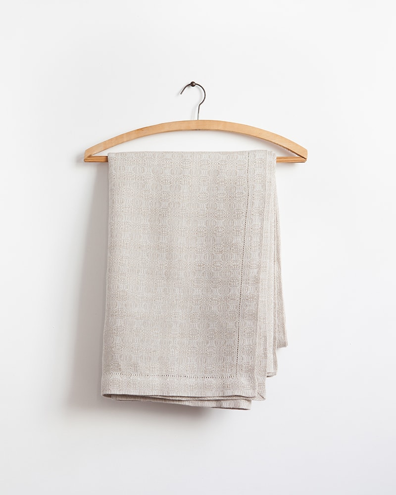 The Mungo Cloverleaf Linen Table Cloth in Natural Flax displayed on a wooden hanger.