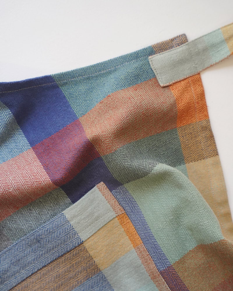 Close up view of the Mungo Alles Apron in Paloma, showcasing its herringbone weave with double pockets and adjustable straps.