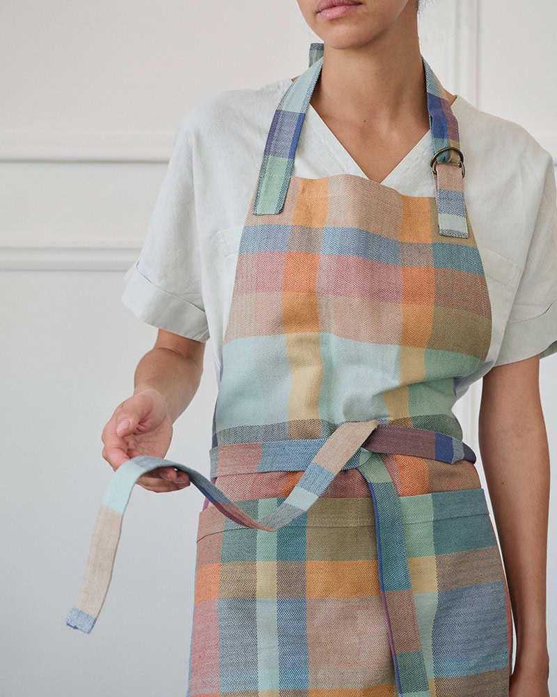 Model standing holding a strap in the Alles Apron in Paloma.