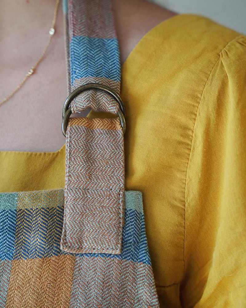 Close up view of the Mungo Alles Apron in Paloma, showcasing its adjustable neck strap with d-ring.
